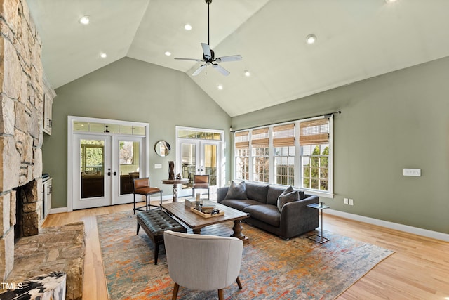 living area featuring baseboards, light wood-style flooring, french doors, a fireplace, and high vaulted ceiling