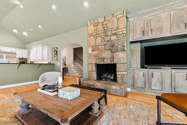 living area featuring arched walkways, light wood finished floors, a fireplace, and baseboards