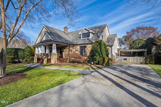 view of front of house with concrete driveway, stone siding, a chimney, covered porch, and a front yard