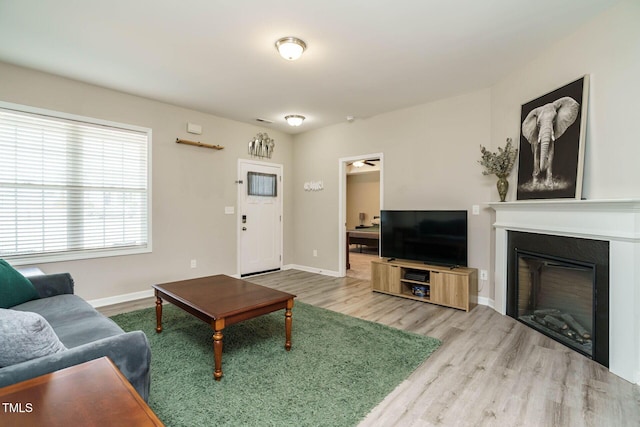 living room with a glass covered fireplace, wood finished floors, visible vents, and baseboards