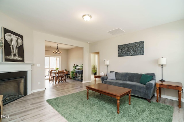 living room featuring visible vents, a glass covered fireplace, wood finished floors, a chandelier, and baseboards