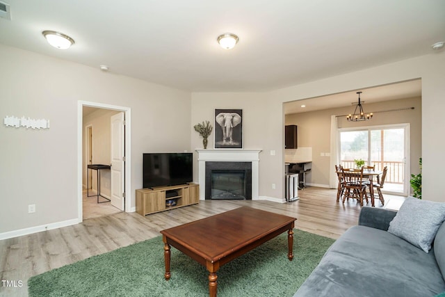 living room featuring visible vents, baseboards, a glass covered fireplace, light wood-style flooring, and a chandelier