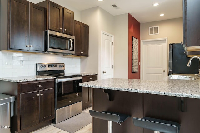 kitchen with a breakfast bar, stainless steel appliances, visible vents, backsplash, and a sink