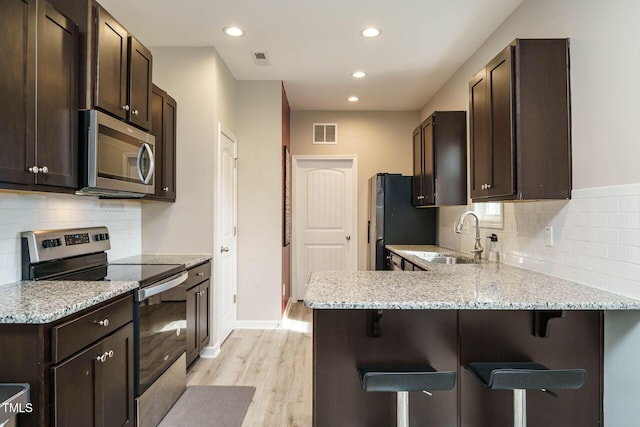 kitchen featuring dark brown cabinetry, visible vents, a breakfast bar, stainless steel appliances, and a sink