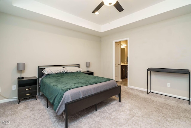 carpeted bedroom featuring ceiling fan, a tray ceiling, ensuite bath, and baseboards