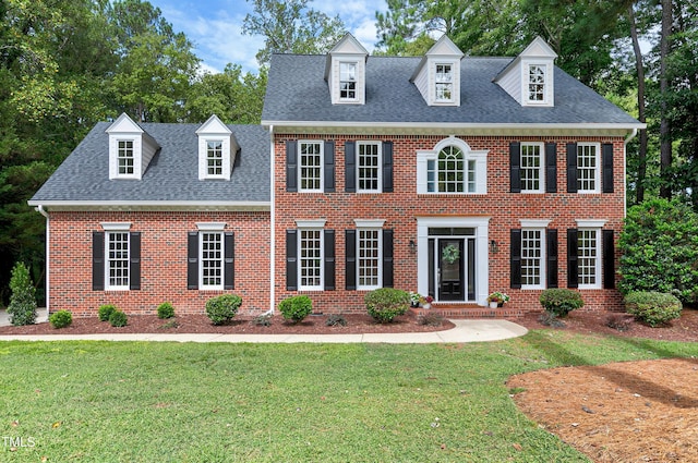 georgian-style home with a shingled roof, brick siding, and a front lawn