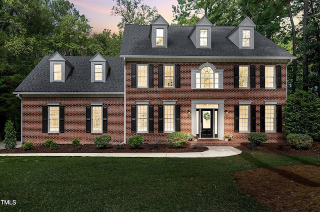 colonial home with a shingled roof, a front yard, and brick siding