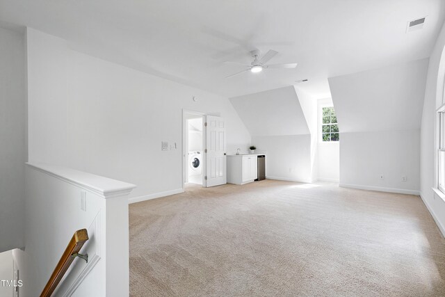 additional living space with visible vents, a ceiling fan, light colored carpet, lofted ceiling, and washer / clothes dryer