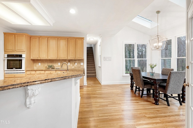 kitchen with light wood-style floors, white oven, light brown cabinets, and backsplash