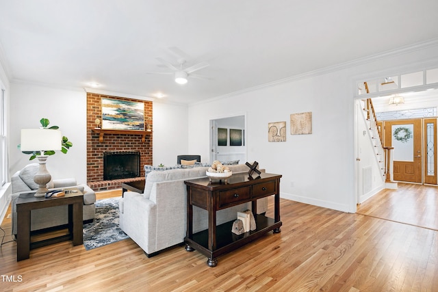 living room with crown molding, light wood-style floors, a ceiling fan, a brick fireplace, and baseboards