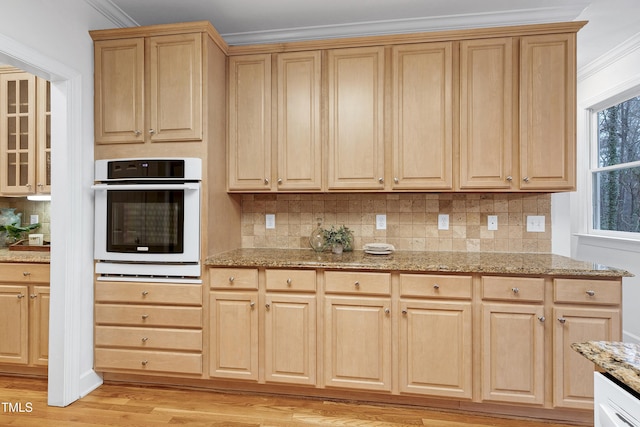 kitchen featuring ornamental molding, oven, light wood-style flooring, and tasteful backsplash