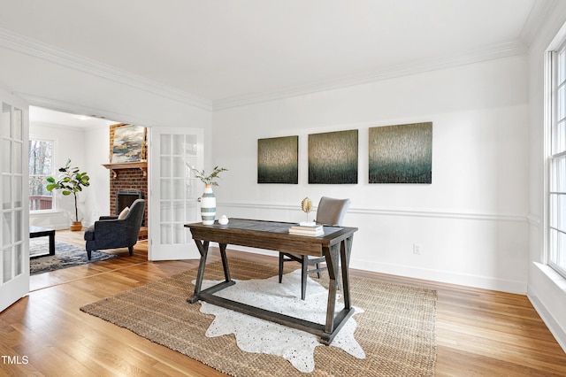 office space featuring ornamental molding, light wood-type flooring, french doors, and a brick fireplace