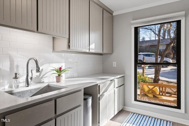 kitchen featuring decorative backsplash, light stone counters, ornamental molding, gray cabinets, and a sink