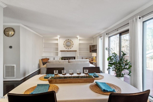 dining area featuring wood finished floors, visible vents, baseboards, a brick fireplace, and crown molding