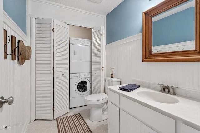 bathroom featuring tile patterned flooring, toilet, vanity, wainscoting, and stacked washing maching and dryer