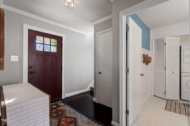 foyer entrance with a textured ceiling, ornamental molding, wood finished floors, and stacked washer and clothes dryer