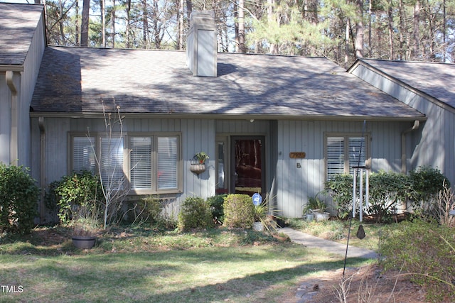 view of front of house with a front yard, roof with shingles, and a chimney