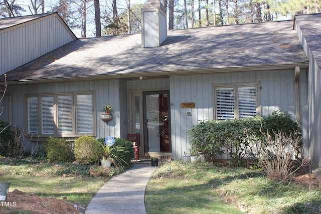 doorway to property featuring a chimney and a shingled roof