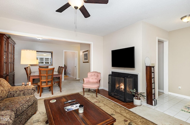 carpeted living room with tile patterned floors, a ceiling fan, a textured ceiling, a glass covered fireplace, and baseboards