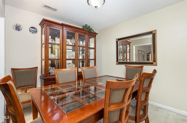 carpeted dining space featuring baseboards, visible vents, and a textured ceiling