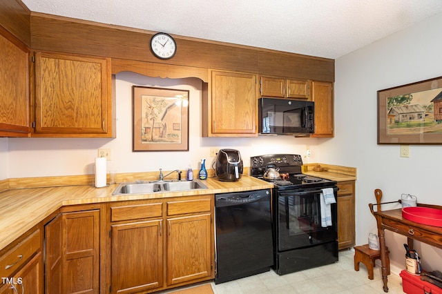 kitchen with a sink, black appliances, light countertops, a textured ceiling, and brown cabinets