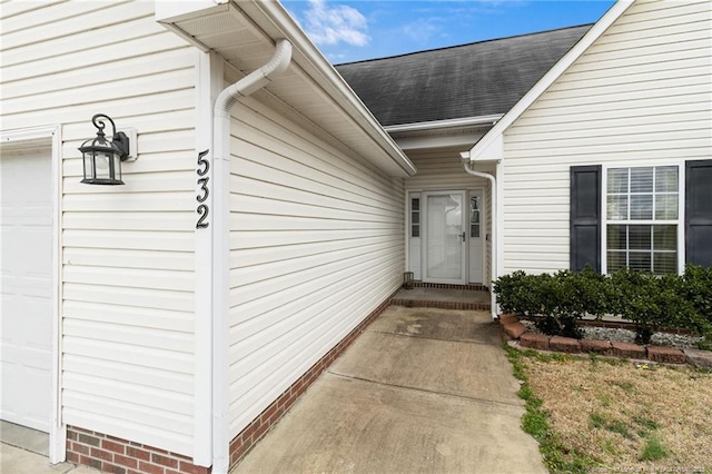 view of exterior entry with a garage and a shingled roof