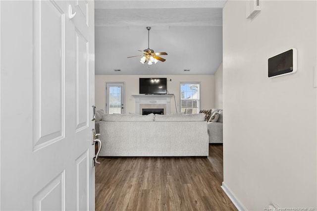 living room featuring baseboards, dark wood finished floors, ceiling fan, vaulted ceiling, and a fireplace