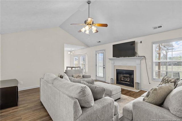 living area featuring visible vents, a fireplace with raised hearth, ceiling fan, wood finished floors, and vaulted ceiling