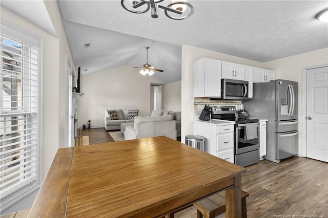 kitchen featuring lofted ceiling, ceiling fan, stainless steel appliances, dark wood-type flooring, and white cabinetry