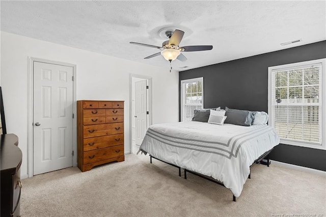 carpeted bedroom with a textured ceiling, baseboards, visible vents, and a ceiling fan