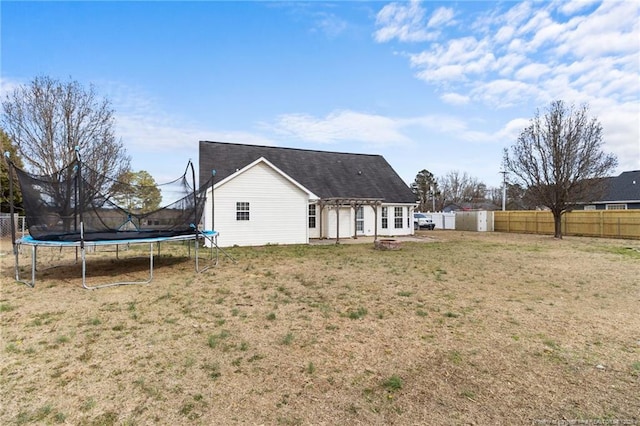 back of house with a trampoline, a patio area, a fenced backyard, and a yard