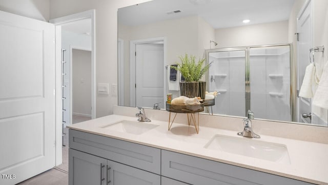 full bathroom featuring double vanity, a stall shower, a sink, and visible vents