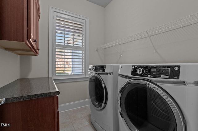 clothes washing area featuring light tile patterned floors, washing machine and dryer, cabinet space, and baseboards