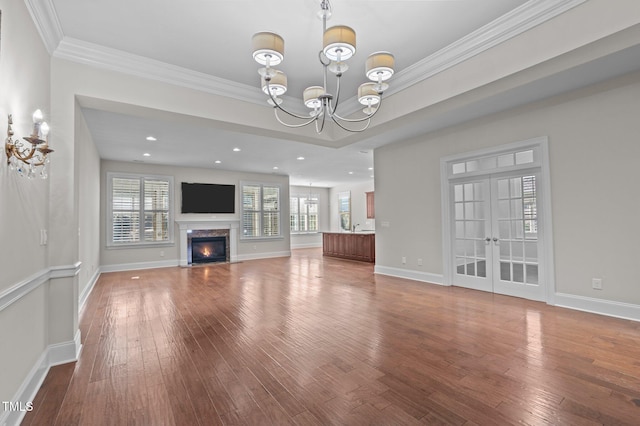 unfurnished living room with baseboards, a chandelier, a premium fireplace, hardwood / wood-style floors, and french doors