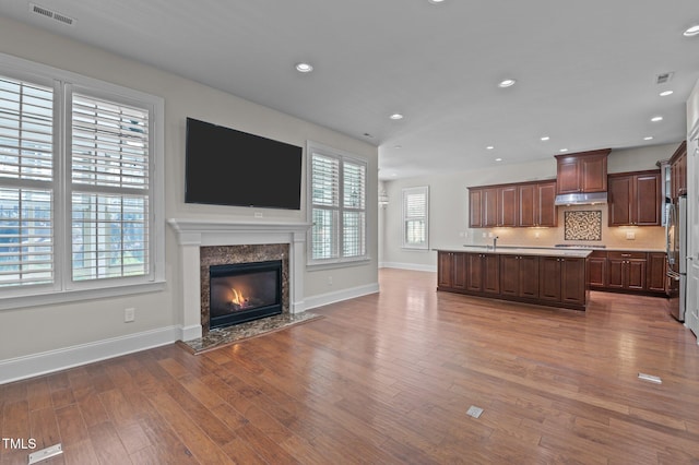 kitchen with visible vents, dark wood-type flooring, a center island with sink, under cabinet range hood, and open floor plan