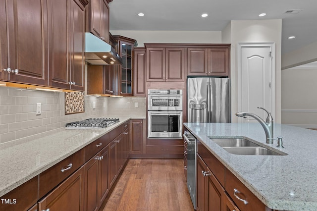 kitchen featuring range hood, light stone countertops, a sink, stainless steel appliances, and light wood-type flooring