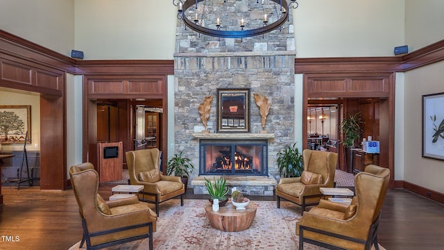 sitting room featuring dark wood finished floors, a high ceiling, a stone fireplace, an inviting chandelier, and baseboards