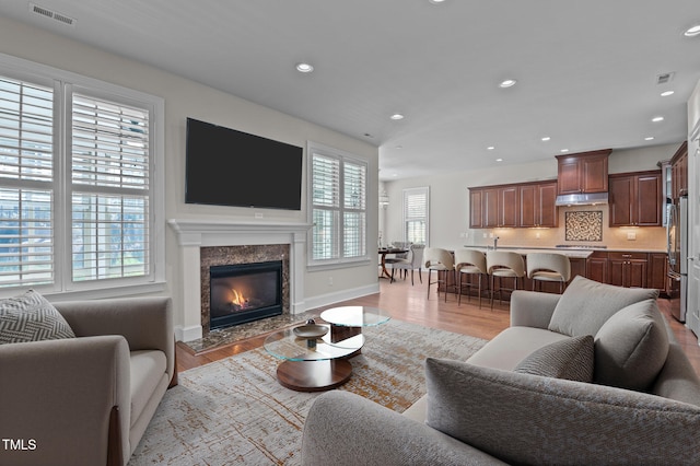 living room with a high end fireplace, visible vents, recessed lighting, and light wood-type flooring