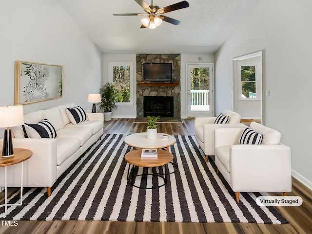 living room with a textured ceiling, a fireplace, wood finished floors, a ceiling fan, and vaulted ceiling