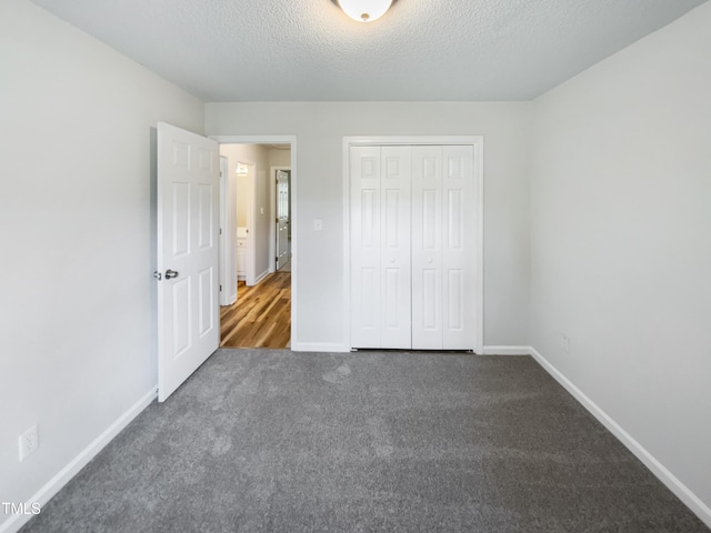 unfurnished bedroom with carpet floors, a closet, a textured ceiling, and baseboards