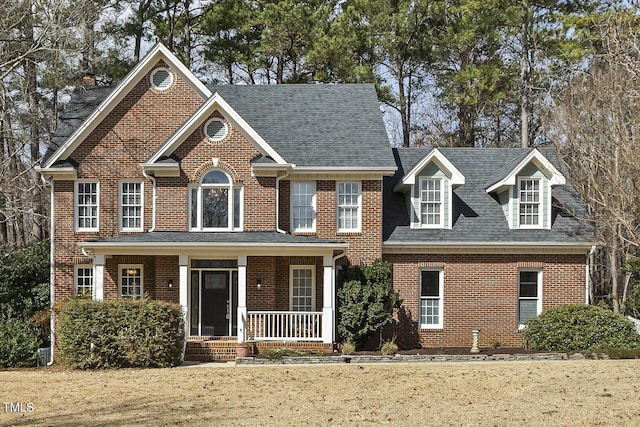 view of front of home featuring a porch, brick siding, and roof with shingles