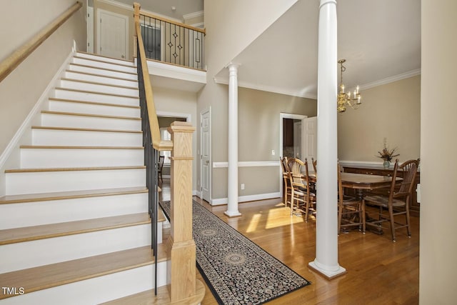 stairway featuring baseboards, wood finished floors, crown molding, ornate columns, and a chandelier