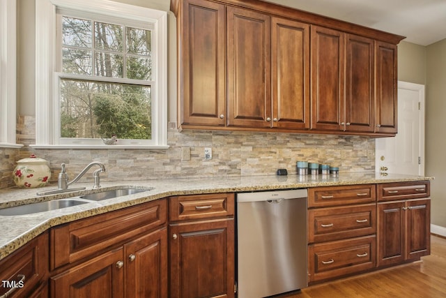 kitchen with wood finished floors, decorative backsplash, stainless steel dishwasher, a sink, and light stone countertops