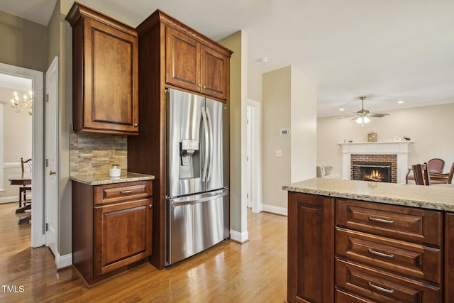 kitchen with light stone counters, stainless steel refrigerator with ice dispenser, backsplash, a brick fireplace, and wood finished floors