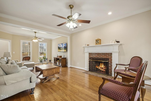 living room featuring light wood-type flooring, a fireplace, baseboards, and crown molding