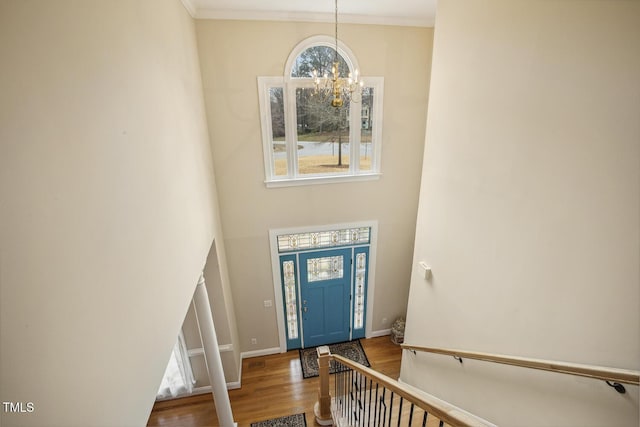 foyer entrance with baseboards, a chandelier, wood finished floors, and ornamental molding