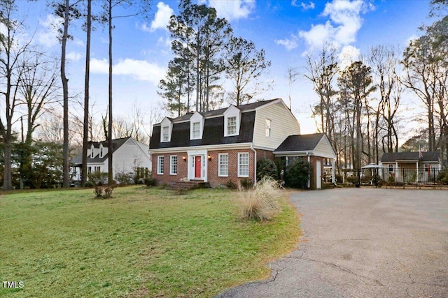 dutch colonial with driveway, a gambrel roof, roof with shingles, a front yard, and brick siding