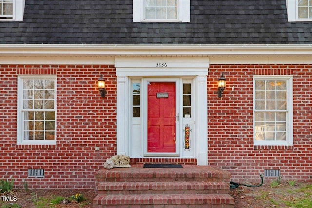 entrance to property featuring crawl space, brick siding, mansard roof, and roof with shingles