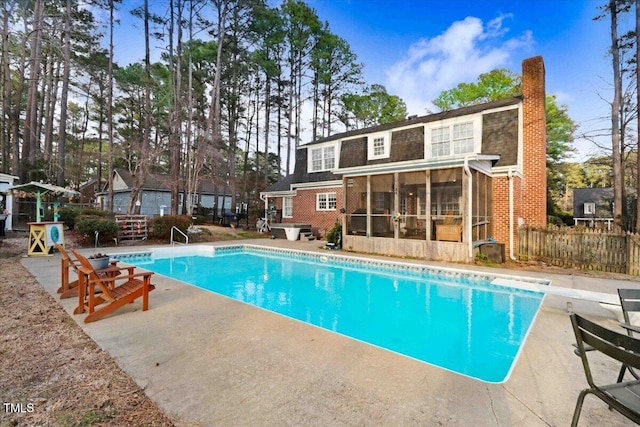 outdoor pool with a sunroom, a patio area, fence, and a diving board