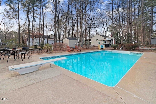 view of pool featuring an outbuilding, fence, a diving board, a fenced in pool, and a patio area